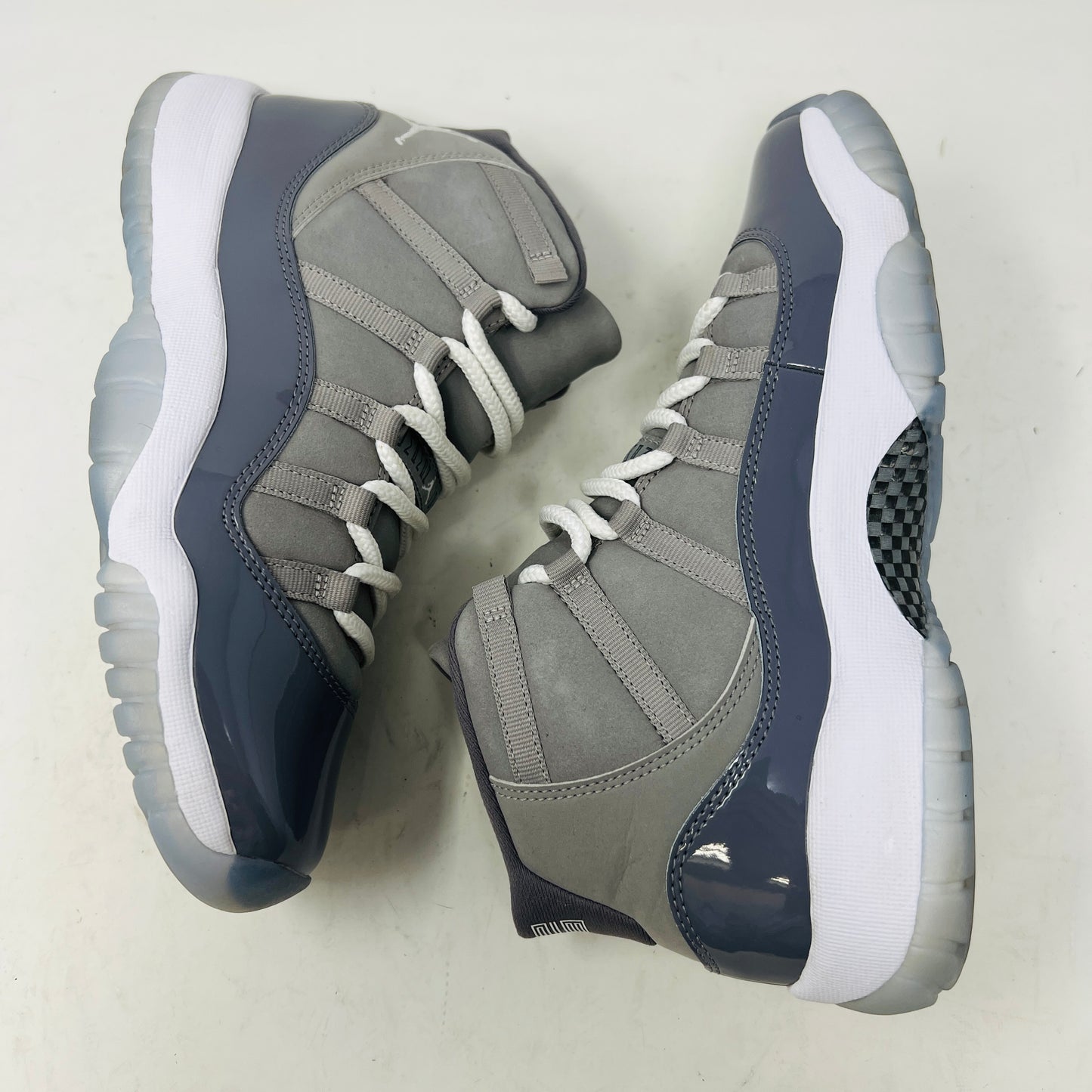 A Jordan 11 Retro Cool Grey (2021) (GS) sneaker by Jordan, in gray and white with a glossy patent leather finish, is displayed on its original Nike shoebox. The box is in good condition featuring a size 6.5Y label and various details, with clean uppers showing light wear and an orange sticker numbered 71.