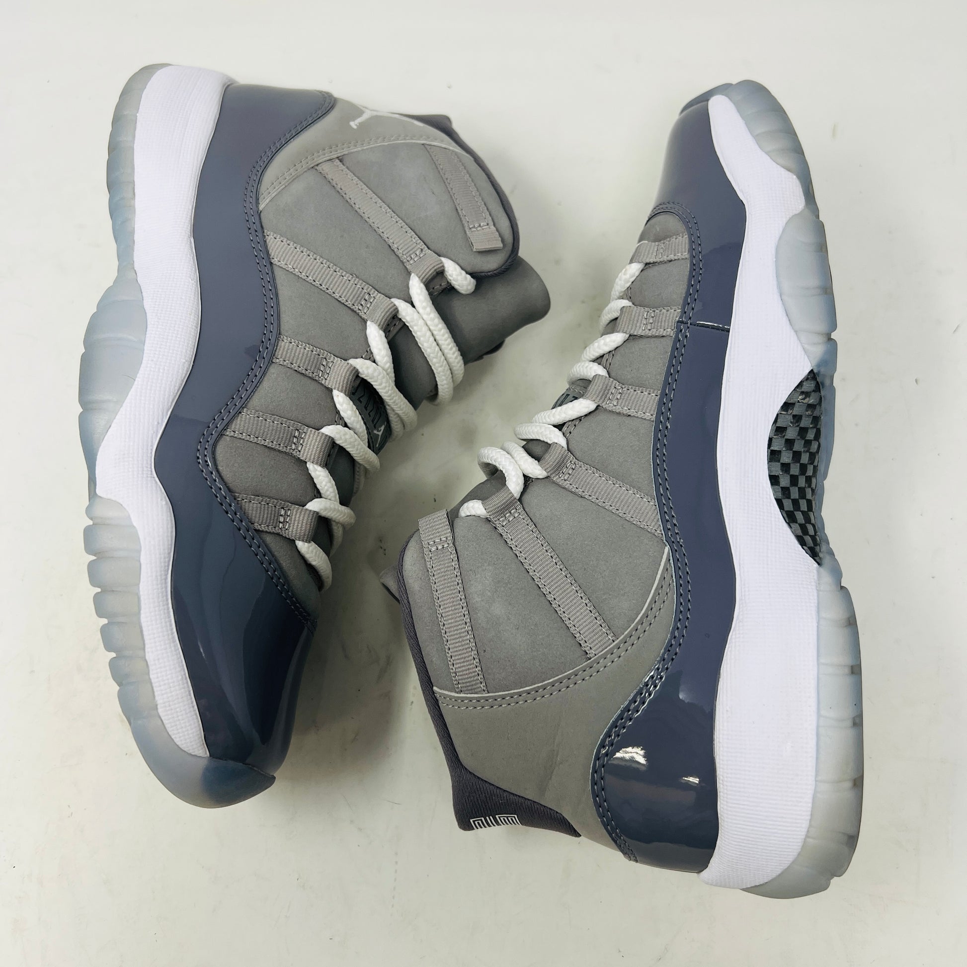 A Jordan 11 Retro Cool Grey (2021) (GS) sneaker by Jordan, in gray and white with a glossy patent leather finish, is displayed on its original Nike shoebox. The box is in good condition featuring a size 6.5Y label and various details, with clean uppers showing light wear and an orange sticker numbered 71.