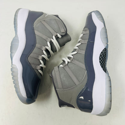 A Jordan 11 Retro Cool Grey (2021) (GS) sneaker by Jordan, in gray and white with a glossy patent leather finish, is displayed on its original Nike shoebox. The box is in good condition featuring a size 6.5Y label and various details, with clean uppers showing light wear and an orange sticker numbered 71.