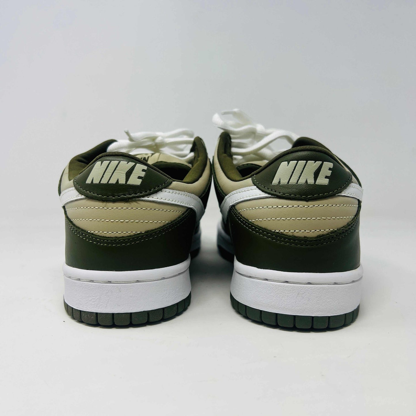 A Nike Dunk Low Light Stone shoe in green and beige with brand new white laces is displayed atop an orange Nike box. Extra white laces are in front, ensuring this 100% authentic pair from the Nike Dunk collection is ready to step out in style.