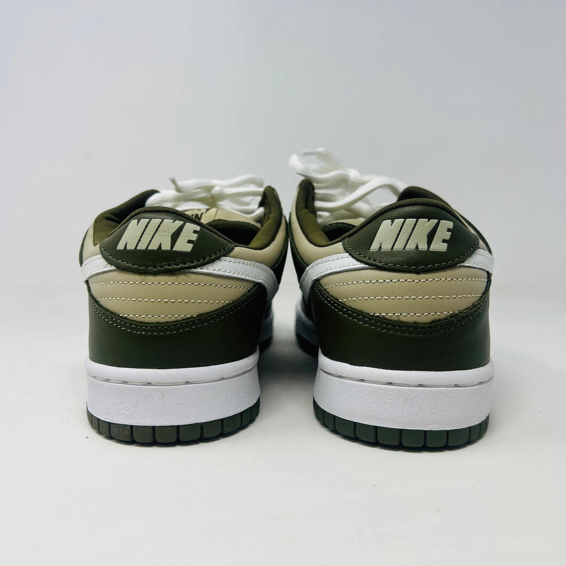 A Nike Dunk Low Light Stone shoe in green and beige with brand new white laces is displayed atop an orange Nike box. Extra white laces are in front, ensuring this 100% authentic pair from the Nike Dunk collection is ready to step out in style.