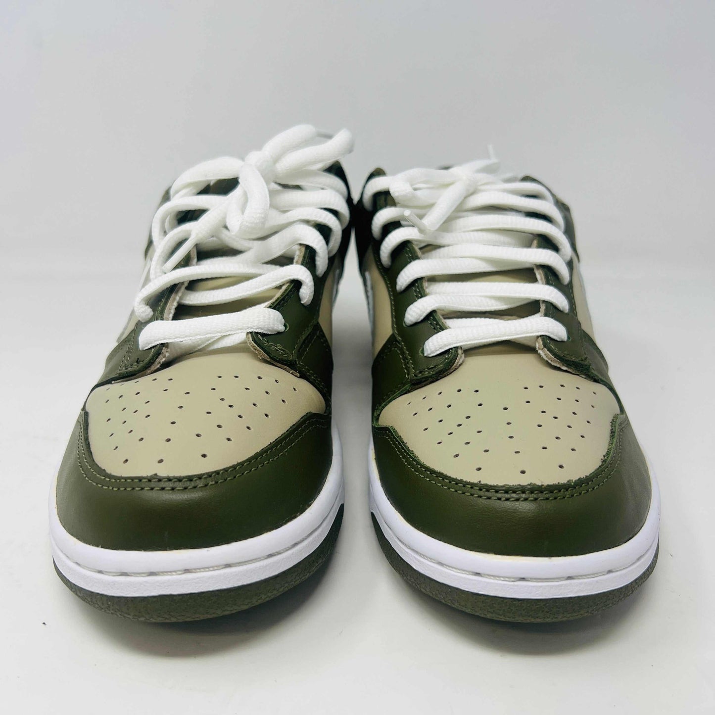 A Nike Dunk Low Light Stone shoe in green and beige with brand new white laces is displayed atop an orange Nike box. Extra white laces are in front, ensuring this 100% authentic pair from the Nike Dunk collection is ready to step out in style.