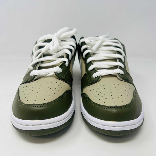 A Nike Dunk Low Light Stone shoe in green and beige with brand new white laces is displayed atop an orange Nike box. Extra white laces are in front, ensuring this 100% authentic pair from the Nike Dunk collection is ready to step out in style.