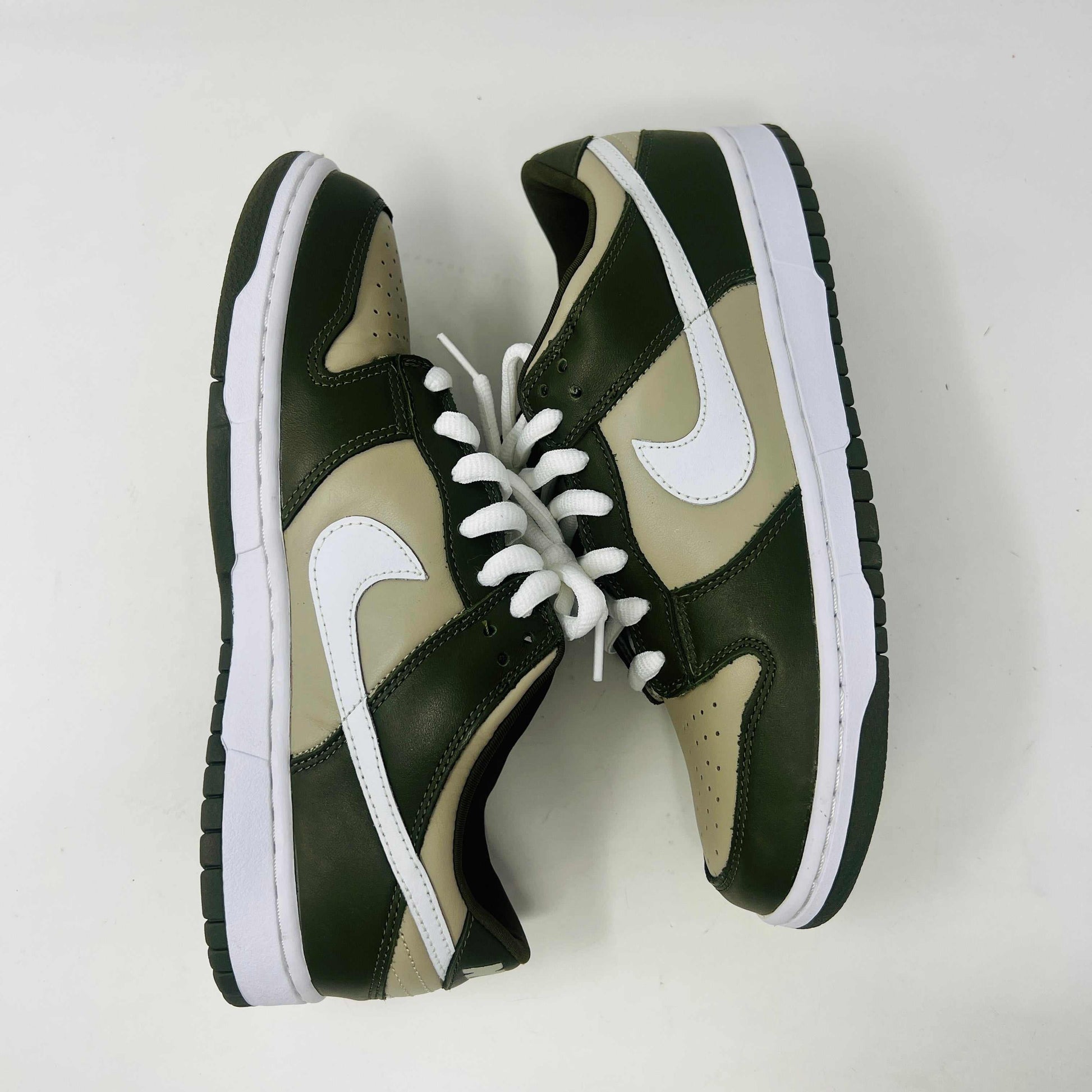 A Nike Dunk Low Light Stone shoe in green and beige with brand new white laces is displayed atop an orange Nike box. Extra white laces are in front, ensuring this 100% authentic pair from the Nike Dunk collection is ready to step out in style.