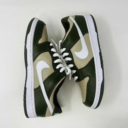 A Nike Dunk Low Light Stone shoe in green and beige with brand new white laces is displayed atop an orange Nike box. Extra white laces are in front, ensuring this 100% authentic pair from the Nike Dunk collection is ready to step out in style.