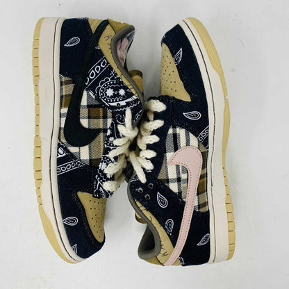The Nike SB Dunk Low Travis Scott sneakers feature beige suede toe caps, black bandana-patterned overlays, white rope laces, authentic pink accents, and a brown label with text on the tongue. Brand new with extra laces, the interior is visible at the top.