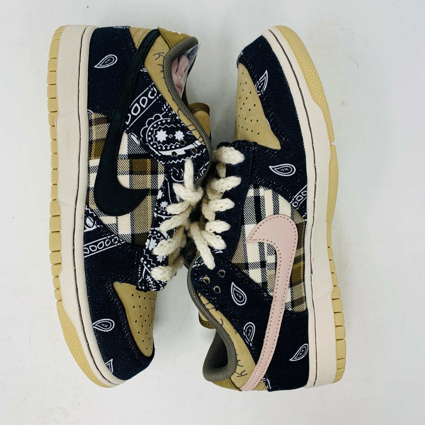 The Nike SB Dunk Low Travis Scott sneakers feature beige suede toe caps, black bandana-patterned overlays, white rope laces, authentic pink accents, and a brown label with text on the tongue. Brand new with extra laces, the interior is visible at the top.