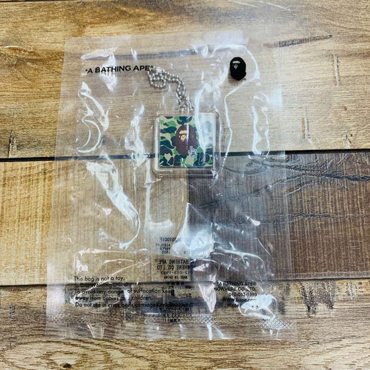 BAPE Ape Head Keychain Green in packaging on wooden surface, brand new.