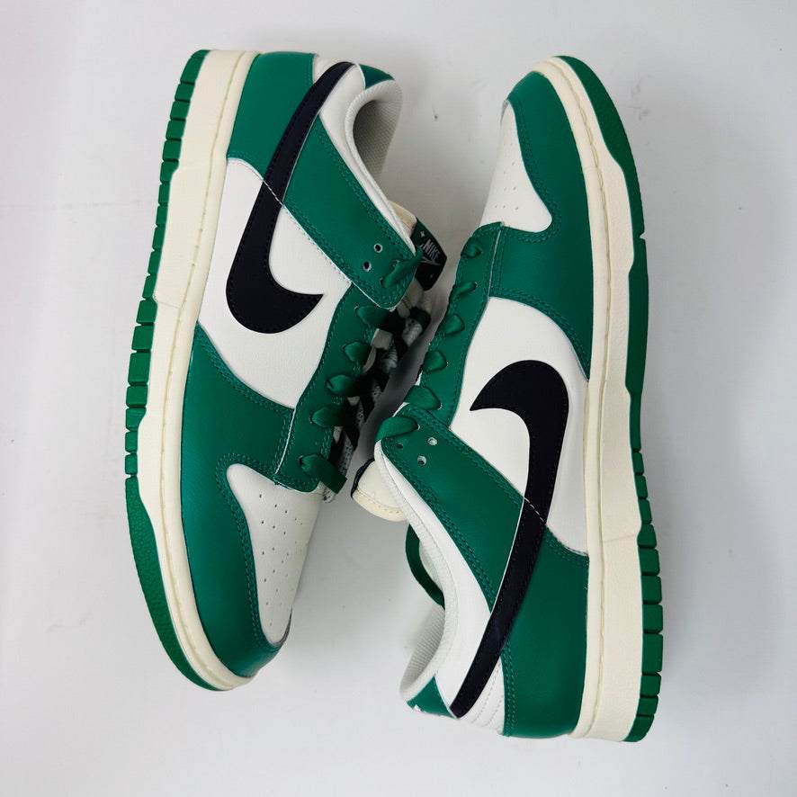 The Nike Dunk Low SE Lottery Pack Malachite Green sneaker, from the 2022 collection, is displayed on a red Nike shoebox. It features clean green and white uppers, a black swoosh logo, and a white midsole. The partially open lid shows essential shoe information and size labels.