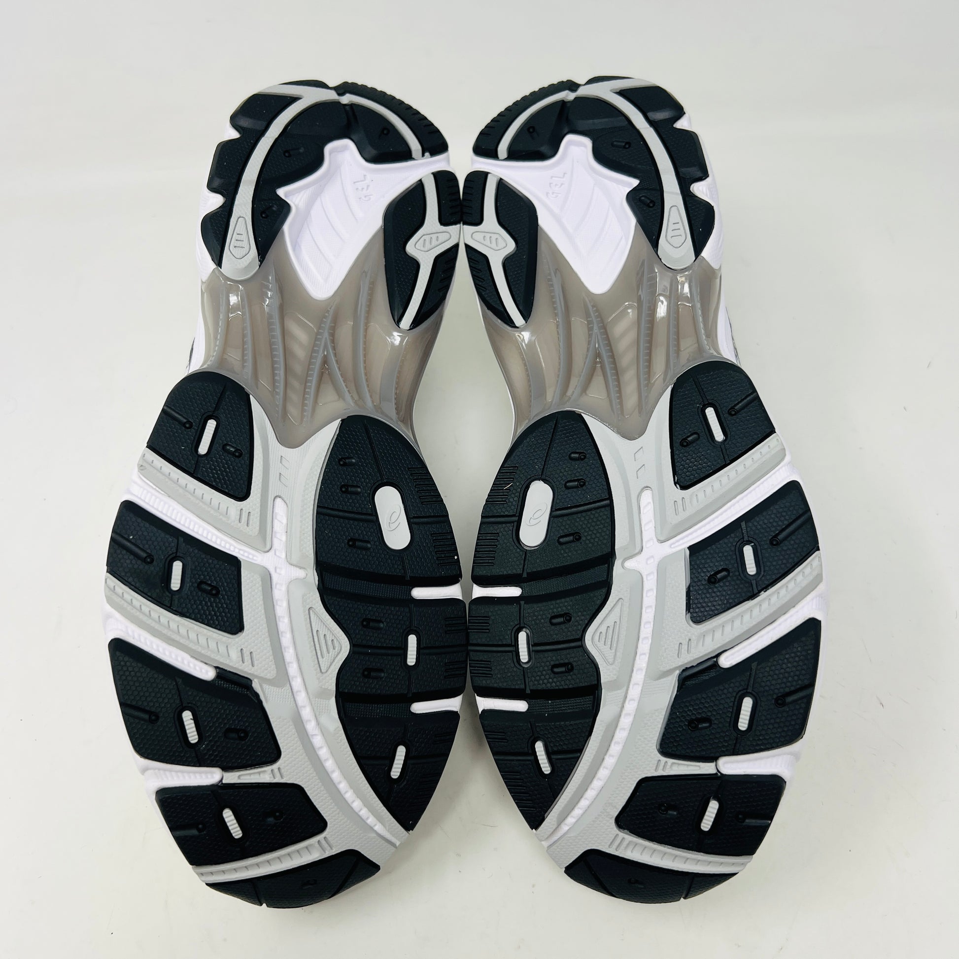 A brand new pair of ASICS GT-2160 JJJJound White sneakers, featuring mesh details and black stripes, is displayed on a black ASICS shoe box with extra laces in front for a complete authentic look.