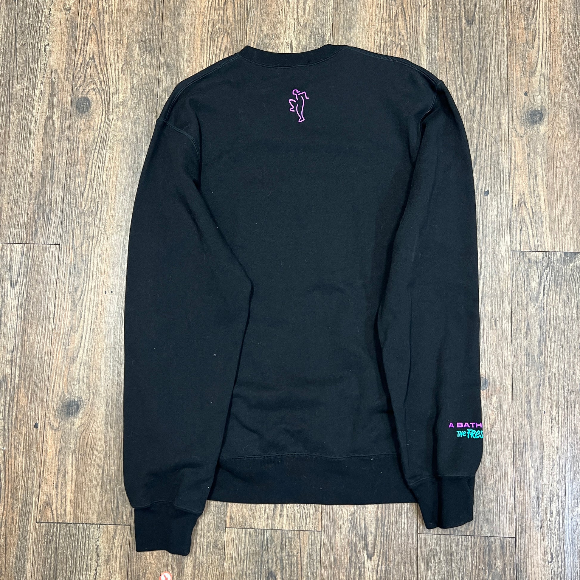 This pre-owned black A BATHING APE X THE FRESH PRINCE sweatshirt by Bape features a vibrant ape graphic with sunglasses, The Fresh Prince in a speech bubble, and purple and green logo accents, all displayed on a wooden floor.