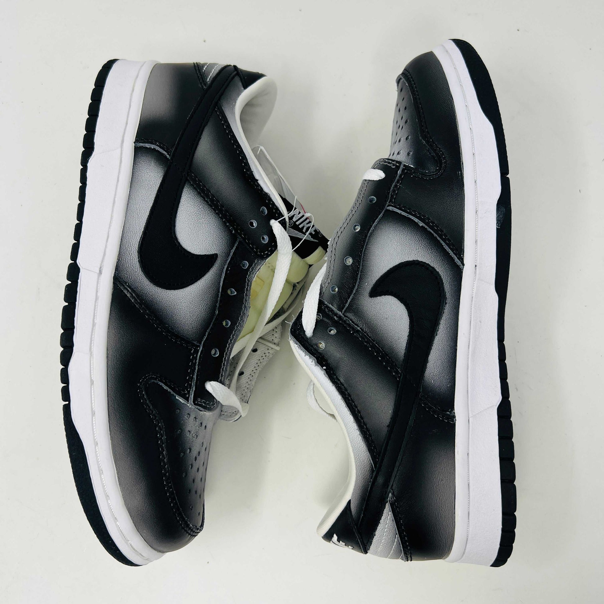 Authentic Nike Dunk Low Haze sneakers in black and white with white laces are displayed front-on against a white backdrop. A clear bag with extra black laces is on the left shoe.