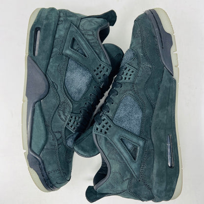 A dark green suede sneaker with a textured design, reminiscent of OG ALL styles, sits atop a matching box. Tagged size 10.5, it features a small red Jumpman logo and includes a XX AIR keychain from its 2017 release. Product: Jordan 4 Retro Kaws Black by Jordan.