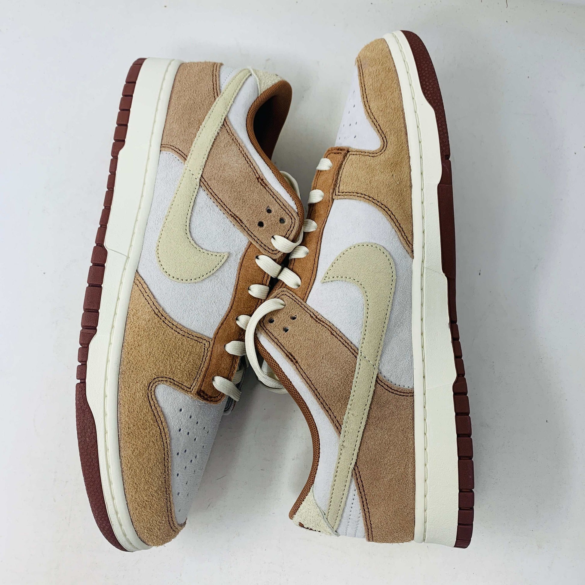A brand new pair of Nike Dunk Low Medium Curry sneakers, with a beige suede upper and white swoosh accents, rests in pristine condition on a red box featuring the bold white Nike logo, set against a plain backdrop.