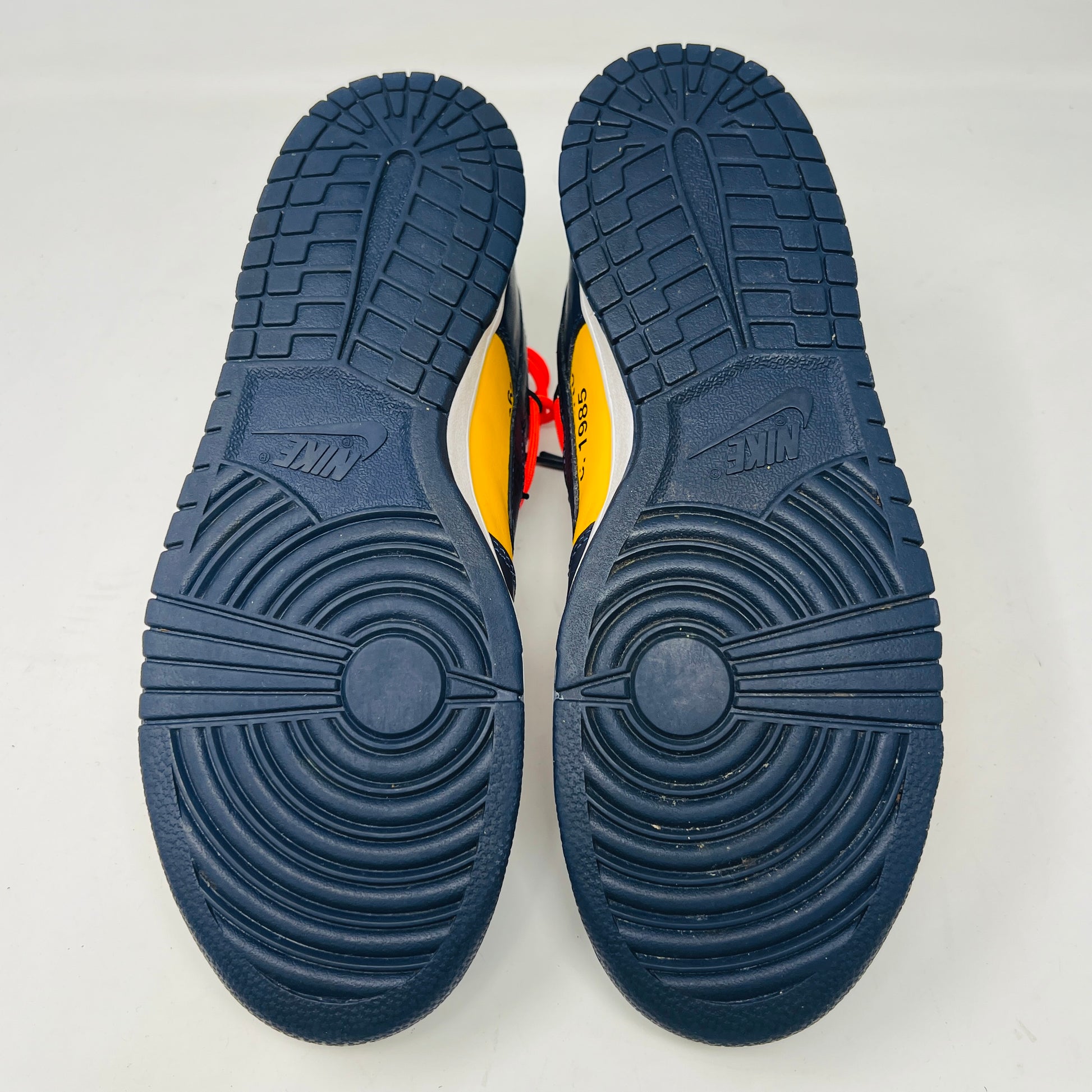 The 2019 Nike Dunk Low Off-White University Gold sneakers feature a navy and yellow design, accented with bold red laces and attached white tags and a zip tie. Displayed atop their box, the label lists them as US size 10.5 and UK size 12, all set against a plain white background.