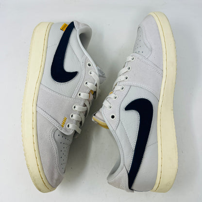 The Jordan 1 Retro AJKO Low SP Union Sail Leather sneakers feature black swooshes, subtle yellow stitching, and white laces. Pictured on a pristine white background, they include extra laces for versatile styling.