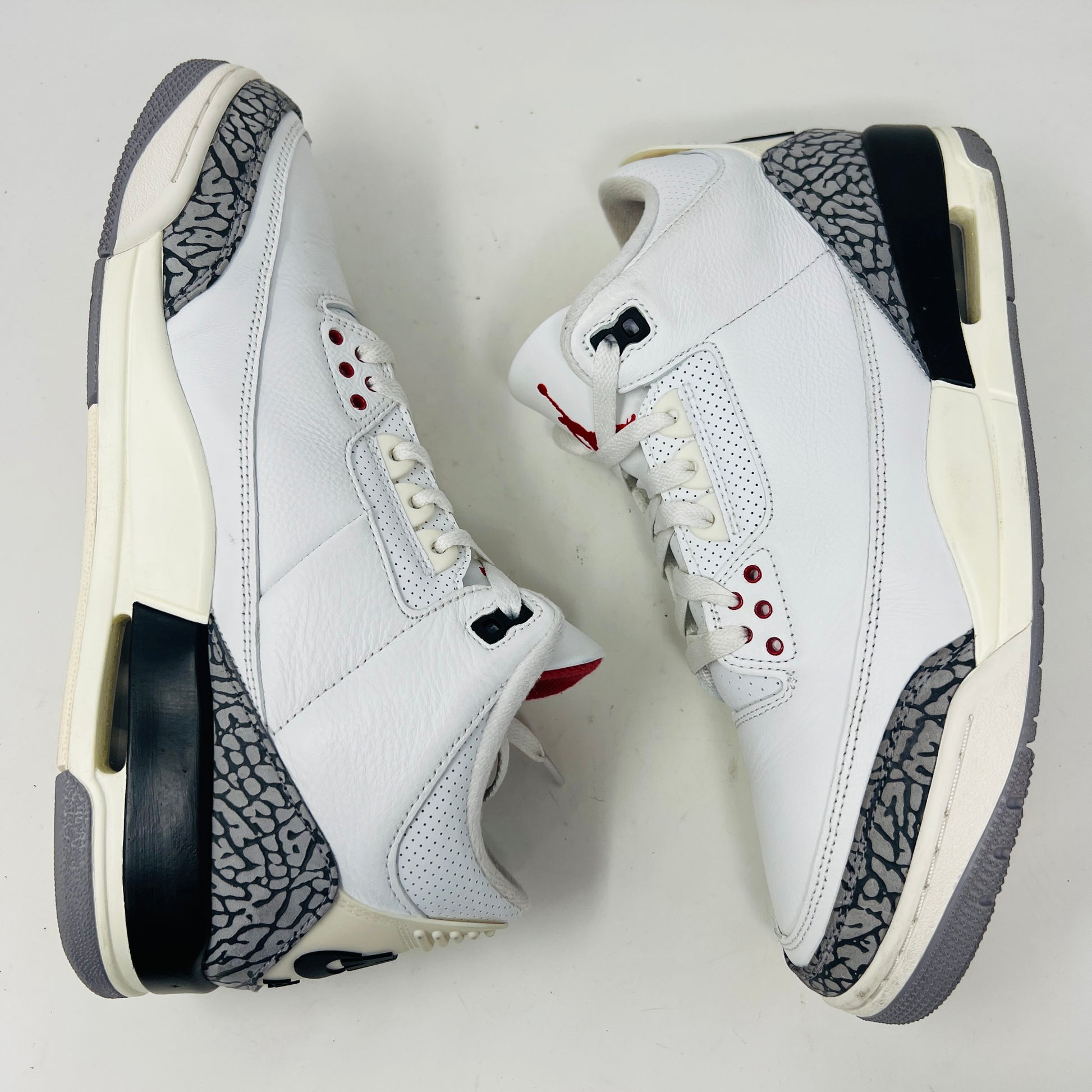 The Jordan 3 Retro White Cement Reimagined features white uppers with gray elephant print and red details, displayed on a black Nike Air shoebox. The size on the box reads 11, and the sneakers are pristine, free from heel drag.