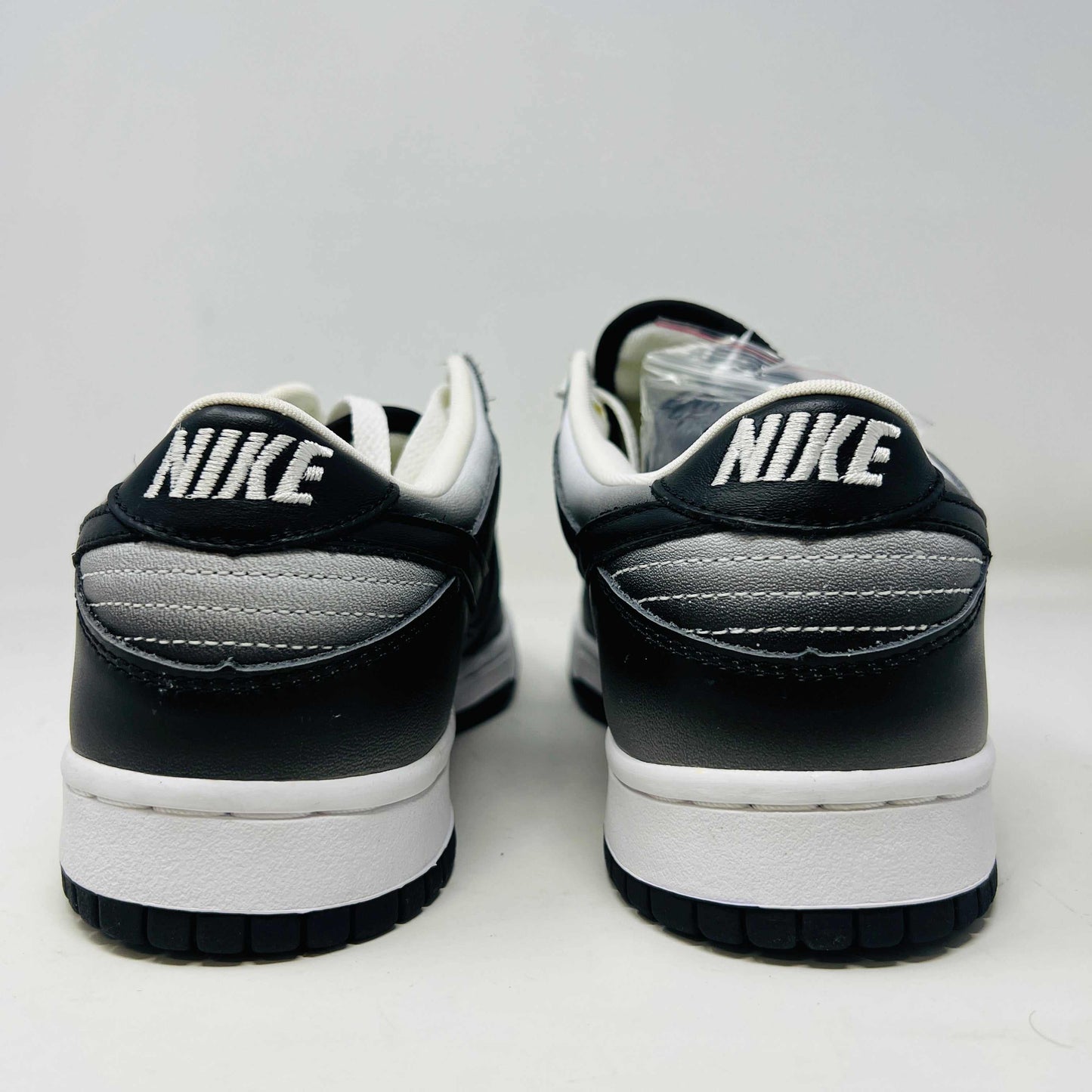 Authentic Nike Dunk Low Haze sneakers in black and white with white laces are displayed front-on against a white backdrop. A clear bag with extra black laces is on the left shoe.