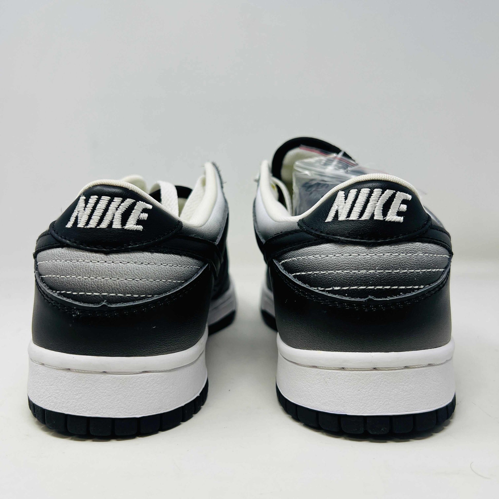 Authentic Nike Dunk Low Haze sneakers in black and white with white laces are displayed front-on against a white backdrop. A clear bag with extra black laces is on the left shoe.