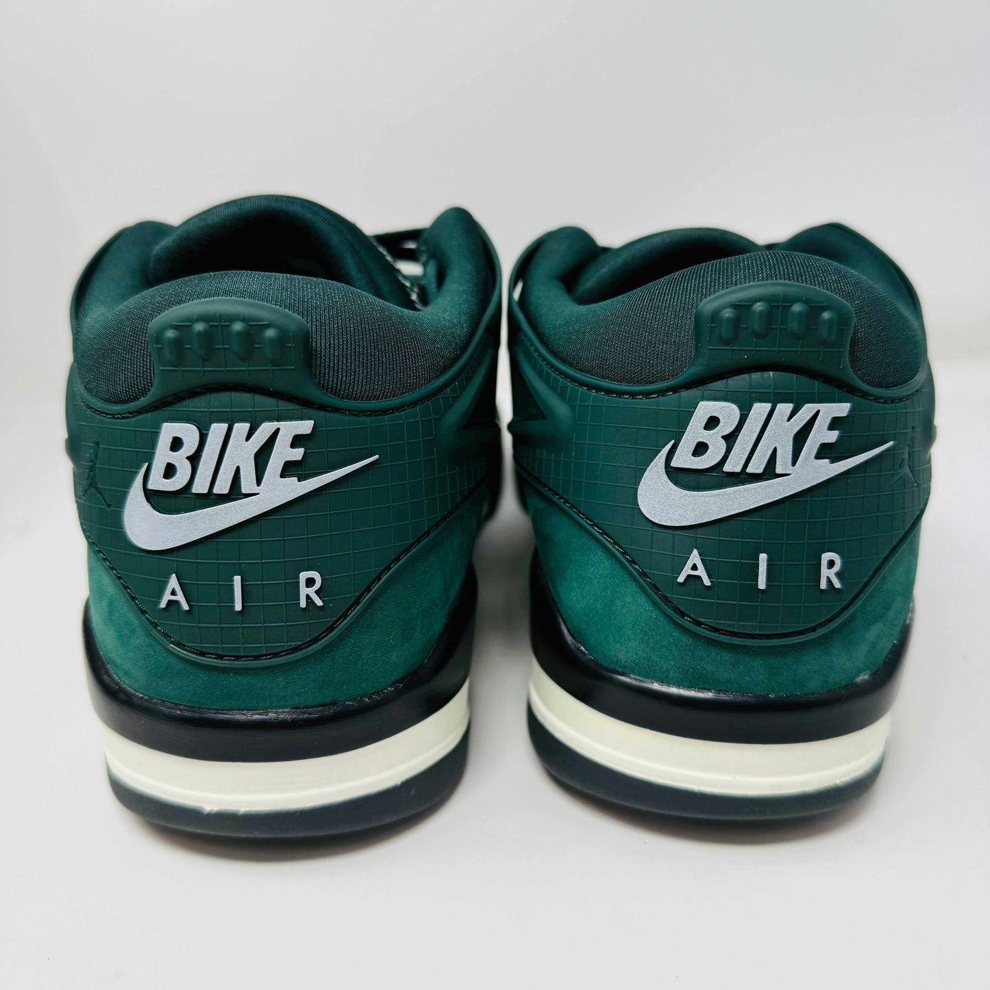 The Jordan 4 RM SP Nigel Sylvester Grandmas Driveway sneakers feature a dark green color with Air by Jordan on the tongue in white, accented with white laces and a low-top design, all set against a plain white background.