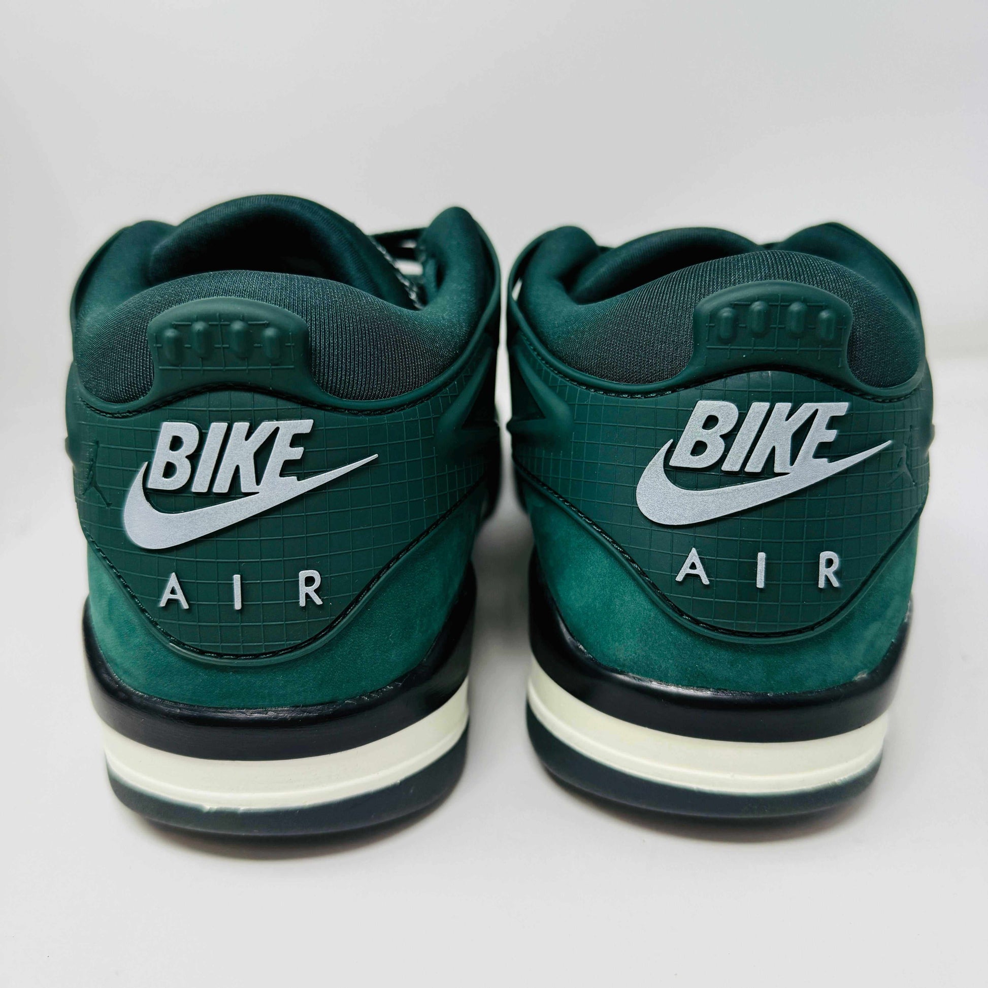 The Jordan 4 RM SP Nigel Sylvester Grandmas Driveway sneakers feature a dark green color with Air by Jordan on the tongue in white, accented with white laces and a low-top design, all set against a plain white background.