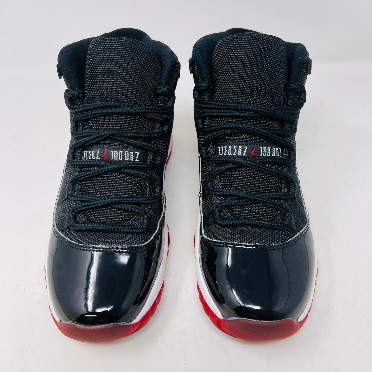 A pristine black and red Jordan 11 Retro Playoffs Bred (2019) (GS) sneaker is on an orange Nike box, featuring a patent leather upper, white midsole, red outsole, and the Jumpman logo near the heel. The label indicates year and size details.