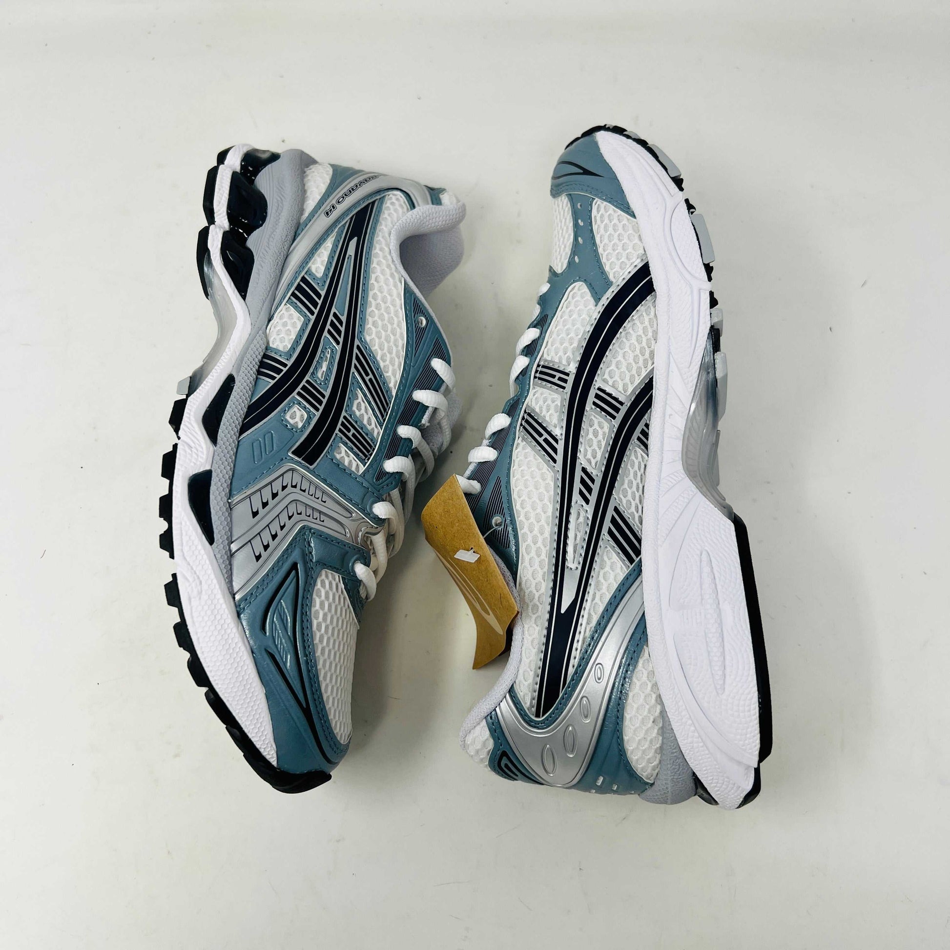 The ASICS Gel-Kayano 14 White Fjord Grey running shoe stands on a brown ASICS box, featuring intricate designs, a breathable mesh upper, and a cushioned thick sole for support. Its 100% authentic.