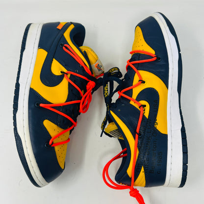 The 2019 Nike Dunk Low Off-White University Gold sneakers feature a navy and yellow design, accented with bold red laces and attached white tags and a zip tie. Displayed atop their box, the label lists them as US size 10.5 and UK size 12, all set against a plain white background.