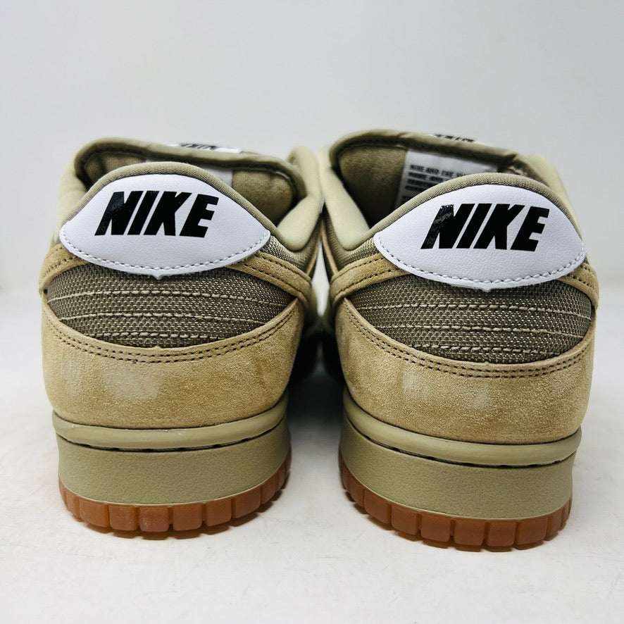 The Nike SB Dunk Low Pro B Parachute Beige, with a beige swoosh and gum sole, is displayed on a purple Nike SB box. New tan suede sneaker includes extra laces neatly rolled up in front against a plain white background.