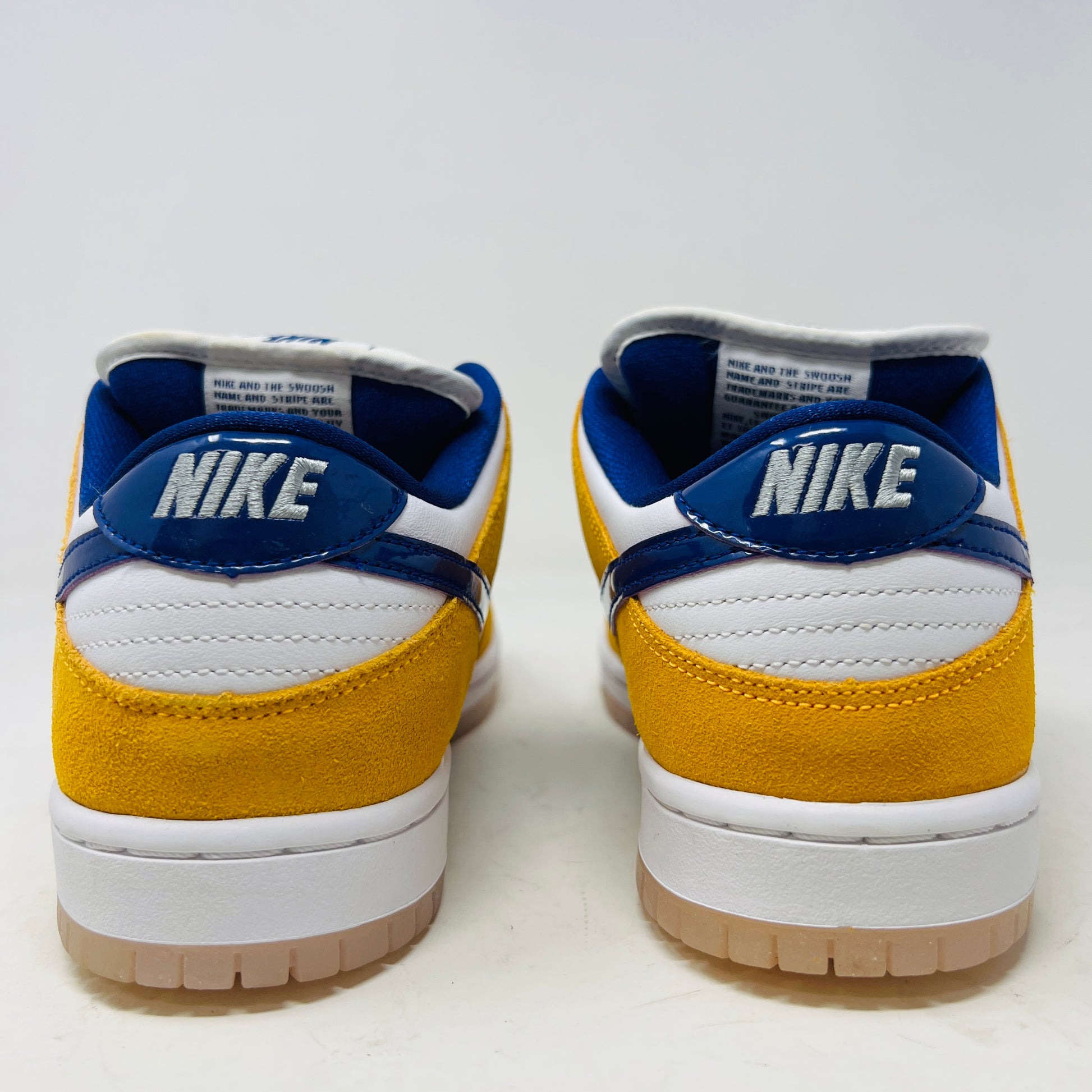 A new Nike SB Dunk Low Laser Orange 8 sneaker, featuring yellow and white suede and leather with a blue swoosh, is displayed on a purple Nike SB box. It includes a white sole, white laces, and extra laces.