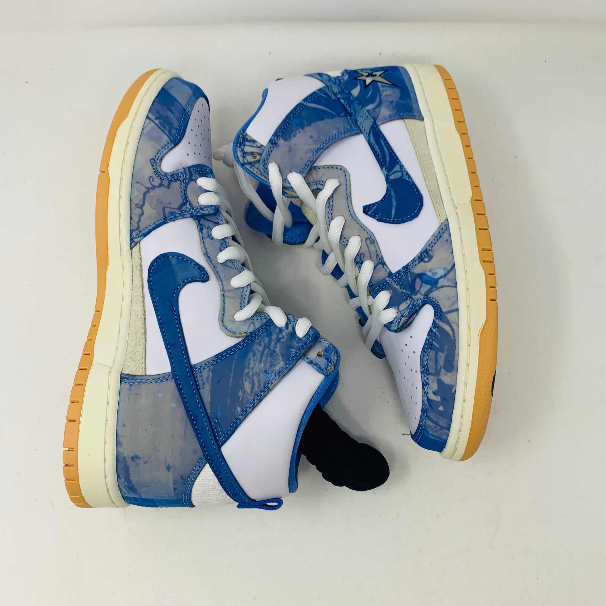 The Nike SB Dunk High Carpet Company sneakers feature a blue and white starry design, presented on a green and yellow Nike shoe box. Three extra laces in blue, yellow, and white are included to ensure your style is 100% authentic.
