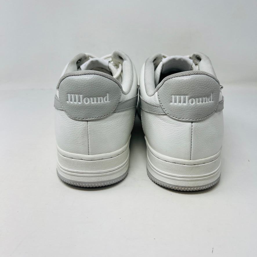 The Bape A Bathing Ape Bape Sta JJJJound white sneaker features clean uppers, a gray star design, and BAPE embossed on its sole. It sits on a camo-patterned box with extra laces from 2022 nearby. Branding includes a monkey face logo and the text A BATHING APE.