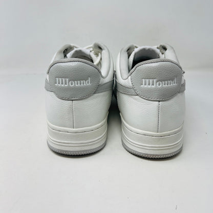The Bape A Bathing Ape Bape Sta JJJJound white sneaker features clean uppers, a gray star design, and BAPE embossed on its sole. It sits on a camo-patterned box with extra laces from 2022 nearby. Branding includes a monkey face logo and the text A BATHING APE.