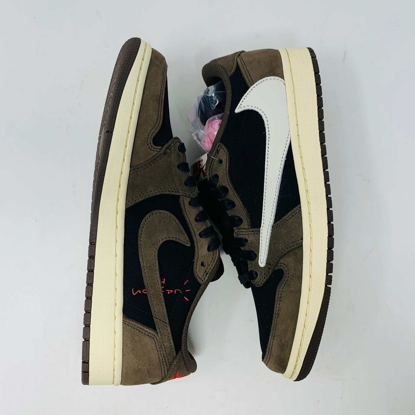 A pair of BRAND NEW Jordan 1 Low OG Travis Scott Mocha sneakers in black and brown, featuring a white swoosh, displayed on a brown shoe box with a red logo. 100% Authentic with EXTRA LACES partially visible inside.
