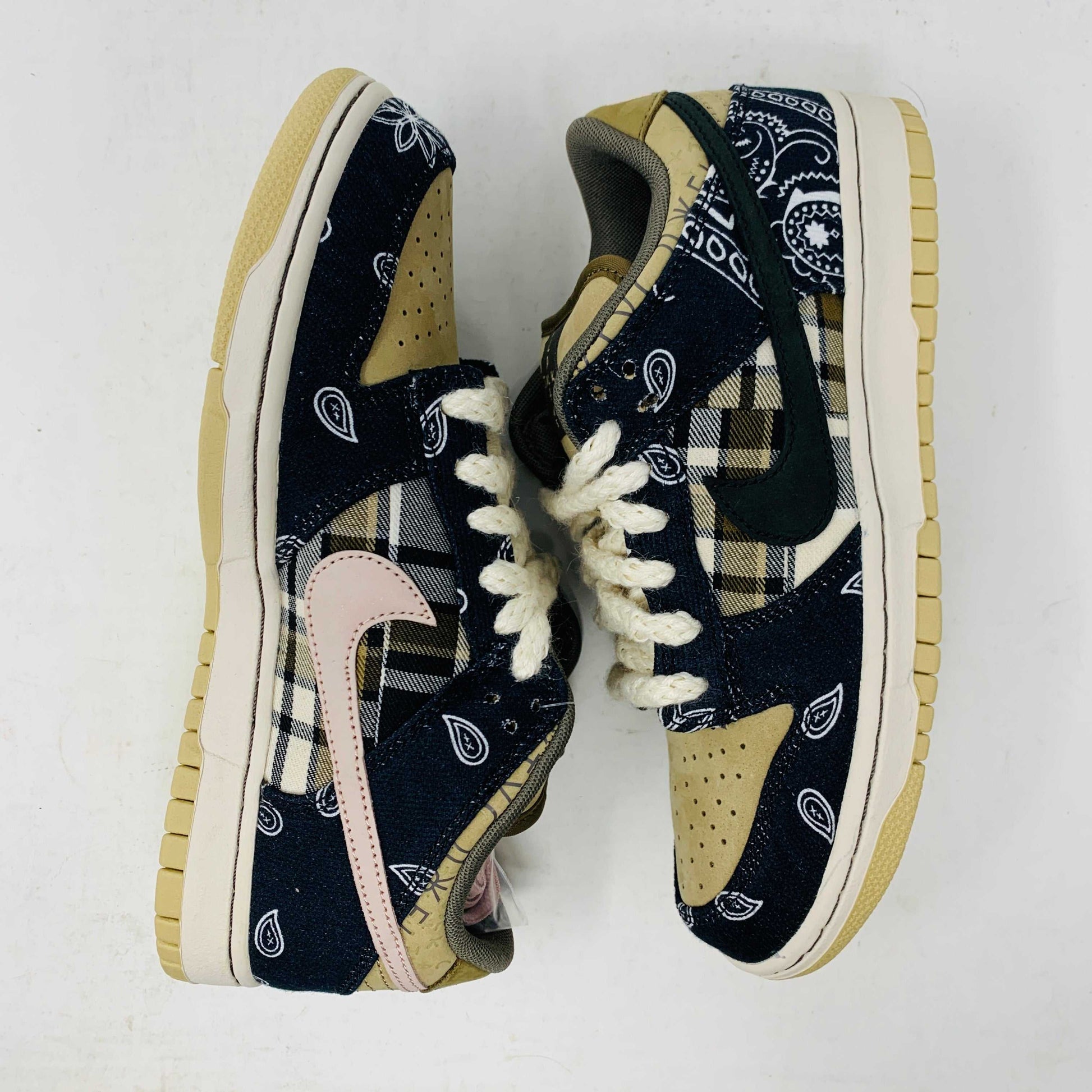 The Nike SB Dunk Low Travis Scott sneakers feature beige suede toe caps, black bandana-patterned overlays, white rope laces, authentic pink accents, and a brown label with text on the tongue. Brand new with extra laces, the interior is visible at the top.