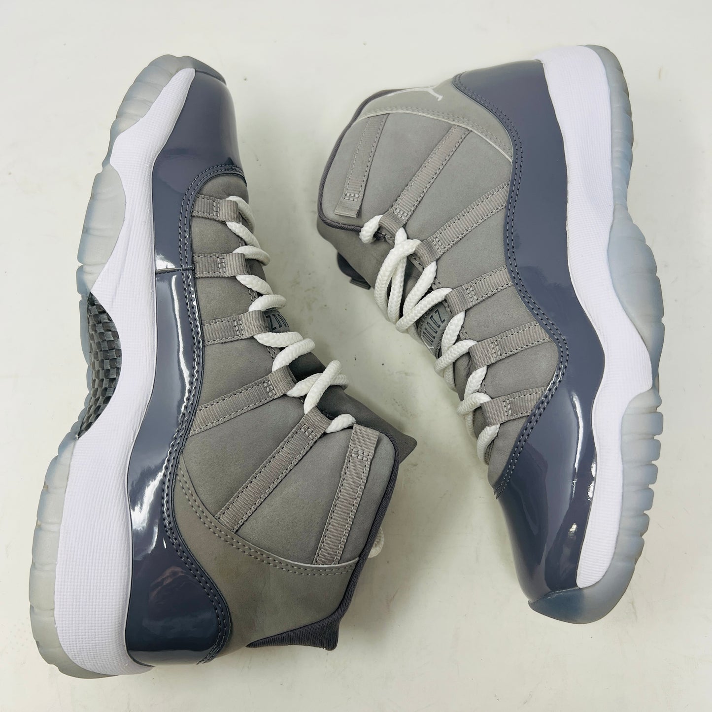 A Jordan 11 Retro Cool Grey (2021) (GS) sneaker by Jordan, in gray and white with a glossy patent leather finish, is displayed on its original Nike shoebox. The box is in good condition featuring a size 6.5Y label and various details, with clean uppers showing light wear and an orange sticker numbered 71.