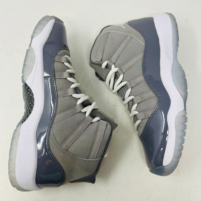 A Jordan 11 Retro Cool Grey (2021) (GS) sneaker by Jordan, in gray and white with a glossy patent leather finish, is displayed on its original Nike shoebox. The box is in good condition featuring a size 6.5Y label and various details, with clean uppers showing light wear and an orange sticker numbered 71.