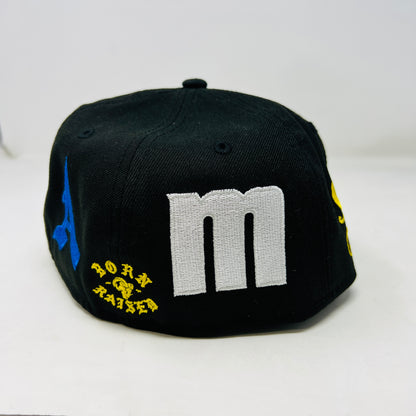 The New Era x Born x Raised x LA RAMS baseball cap by born x raised features LA in yellow and white embroidery on the front. It has a size 7 1/2 sticker on the brim with yellow and blue side patches, all set against a plain white background for a bold statement.