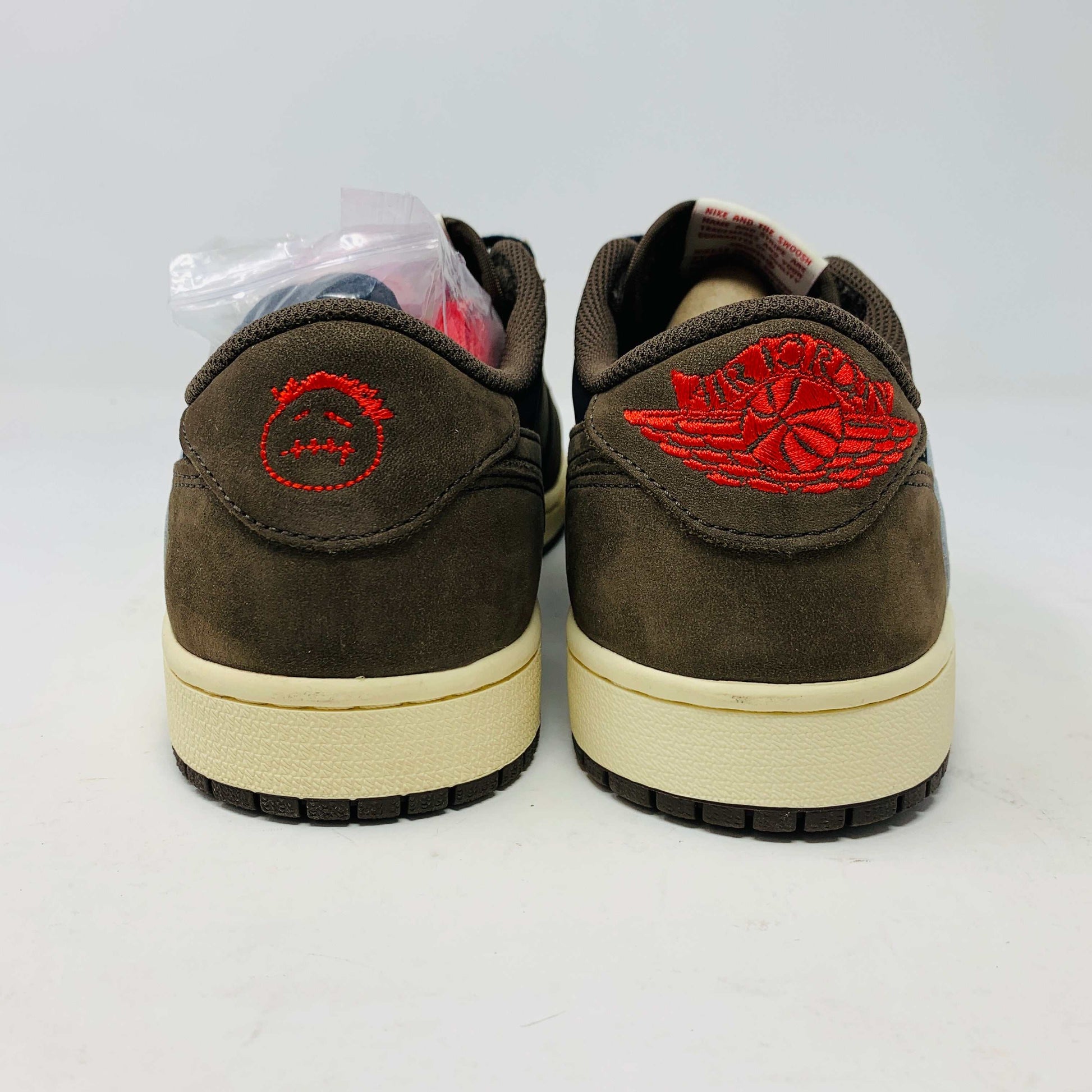 A pair of BRAND NEW Jordan 1 Low OG Travis Scott Mocha sneakers in black and brown, featuring a white swoosh, displayed on a brown shoe box with a red logo. 100% Authentic with EXTRA LACES partially visible inside.