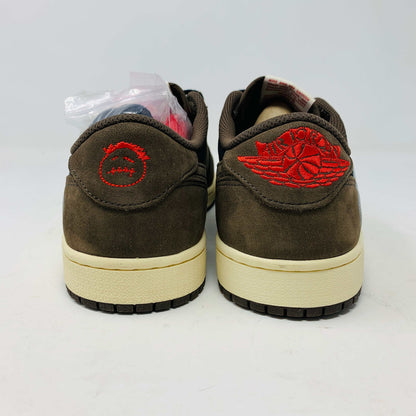 A pair of BRAND NEW Jordan 1 Low OG Travis Scott Mocha sneakers in black and brown, featuring a white swoosh, displayed on a brown shoe box with a red logo. 100% Authentic with EXTRA LACES partially visible inside.