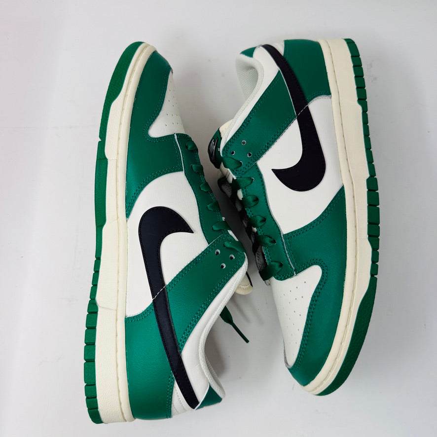 The Nike Dunk Low SE Lottery Pack Malachite Green sneaker, from the 2022 collection, is displayed on a red Nike shoebox. It features clean green and white uppers, a black swoosh logo, and a white midsole. The partially open lid shows essential shoe information and size labels.
