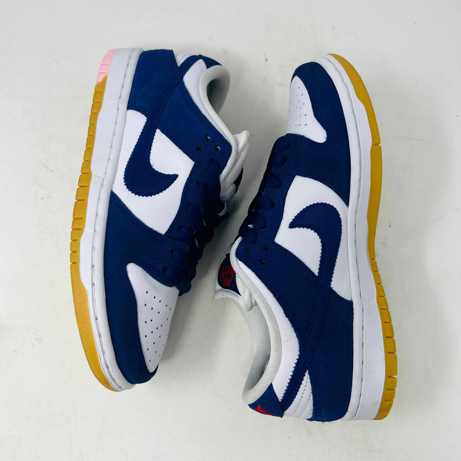 A blue and white Nike SB Dunk Low Los Angeles Dodgers sneaker, complete with a gum sole, sits on a purple box labeled for sizes 5 and 6.5. Beside it are coiled laces in white, blue, and red for that twice-worn look.