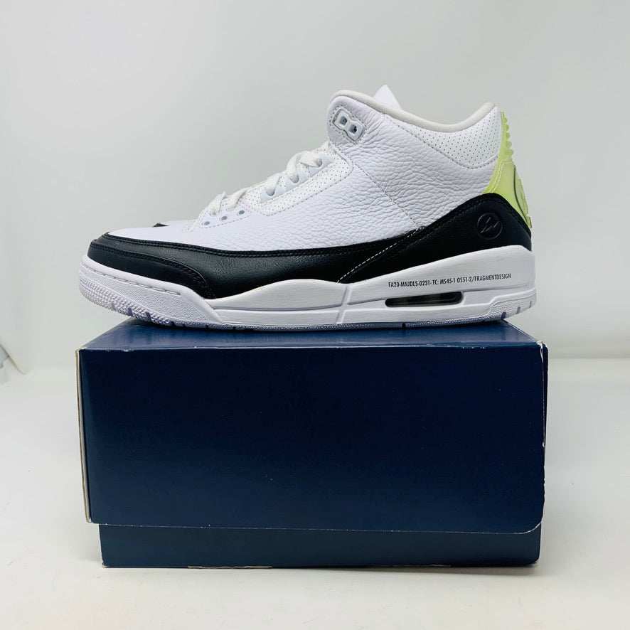 The Jordan 3 Fragment by Jordan, a white sneaker with black midsole and lime green heel detailing, is displayed on a closed blue shoebox.