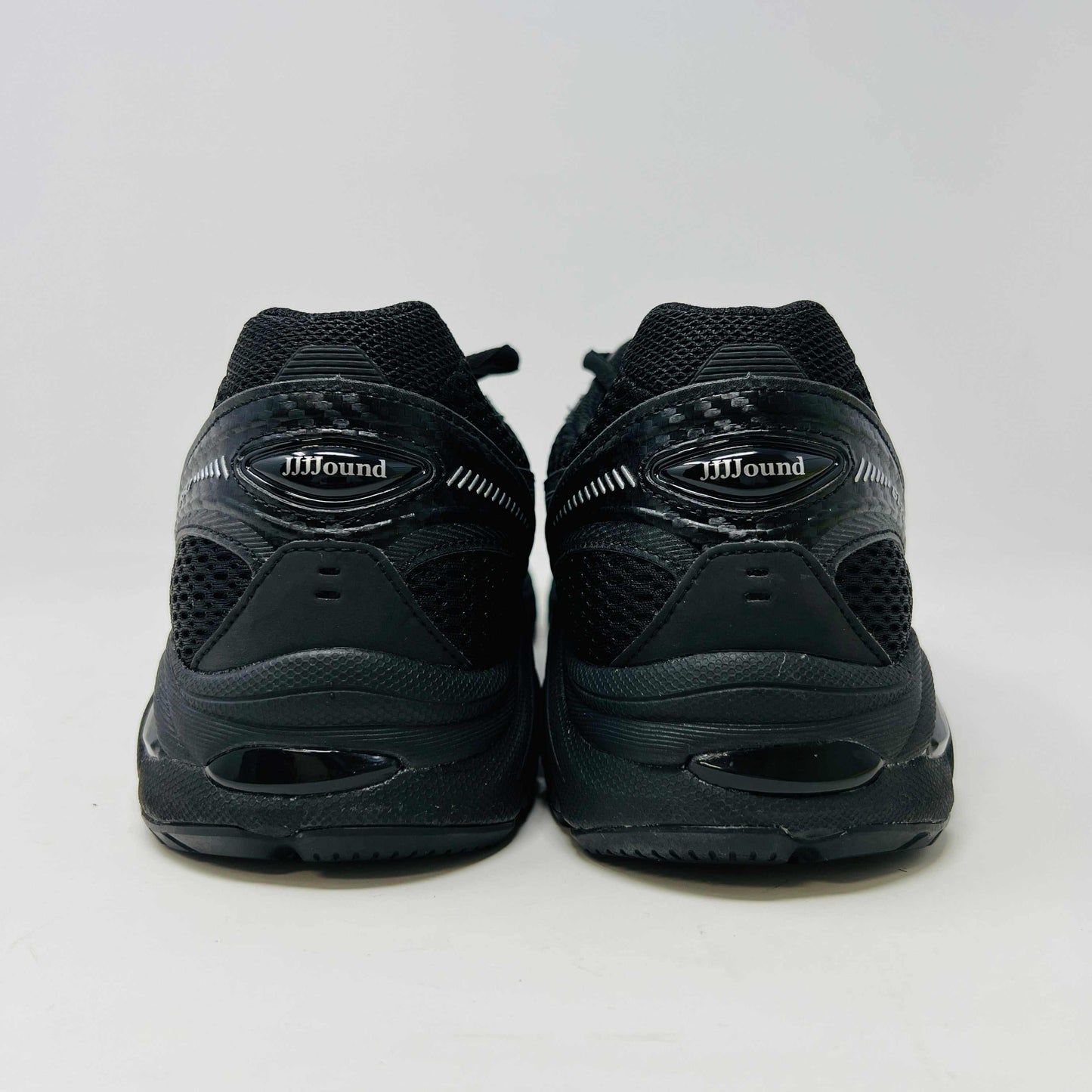 The new ASICS GT-2160 JJJJound Black running shoe sits on its box, featuring extra laces in a clear bag. These authentic shoes present a sleek design with gray detailing and a side text label.
