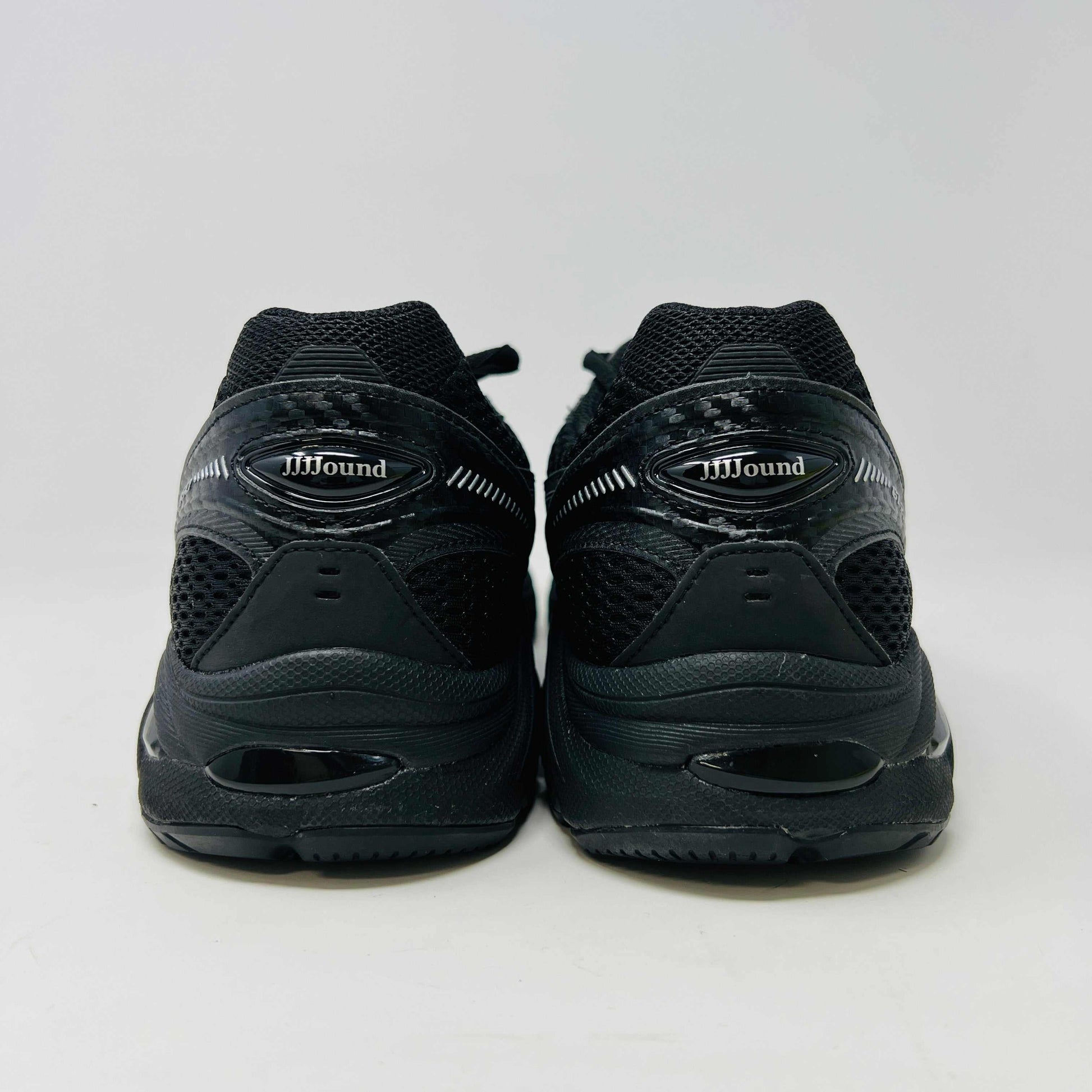 The new ASICS GT-2160 JJJJound Black running shoe sits on its box, featuring extra laces in a clear bag. These authentic shoes present a sleek design with gray detailing and a side text label.