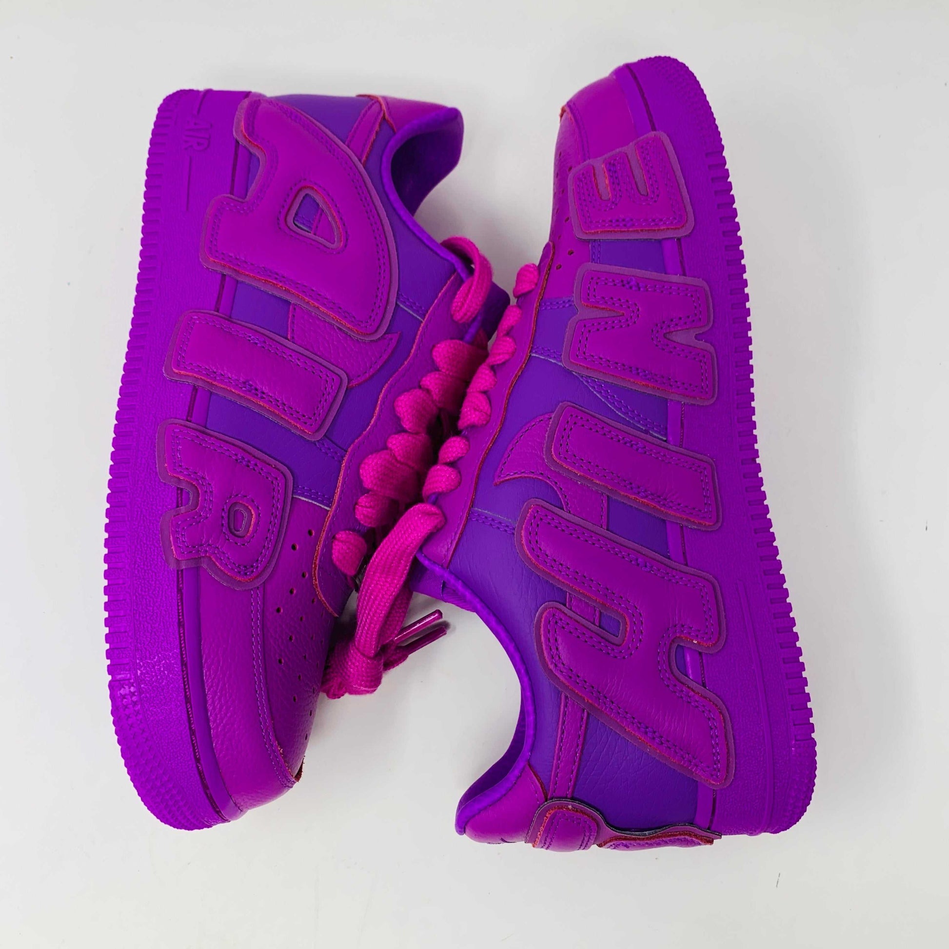 The Nike Air Force 1 Low Cactus Plant Flea Market Fuchsia Dream sneaker, vibrant pink with oversized SUN lettering, boldly sits on a black box featuring the iconic white swoosh. This brand new, 100% authentic pair includes extra laces and is presented against a plain white background.