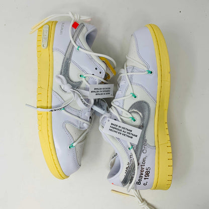 The Nike Dunk Low Off White Lot 1 sneaker, white with a metallic silver swoosh and vibrant accents, rests on a brown shoebox. Its unique lace design and 01 of 50 detailing highlight its 2021 release against a plain white backdrop.