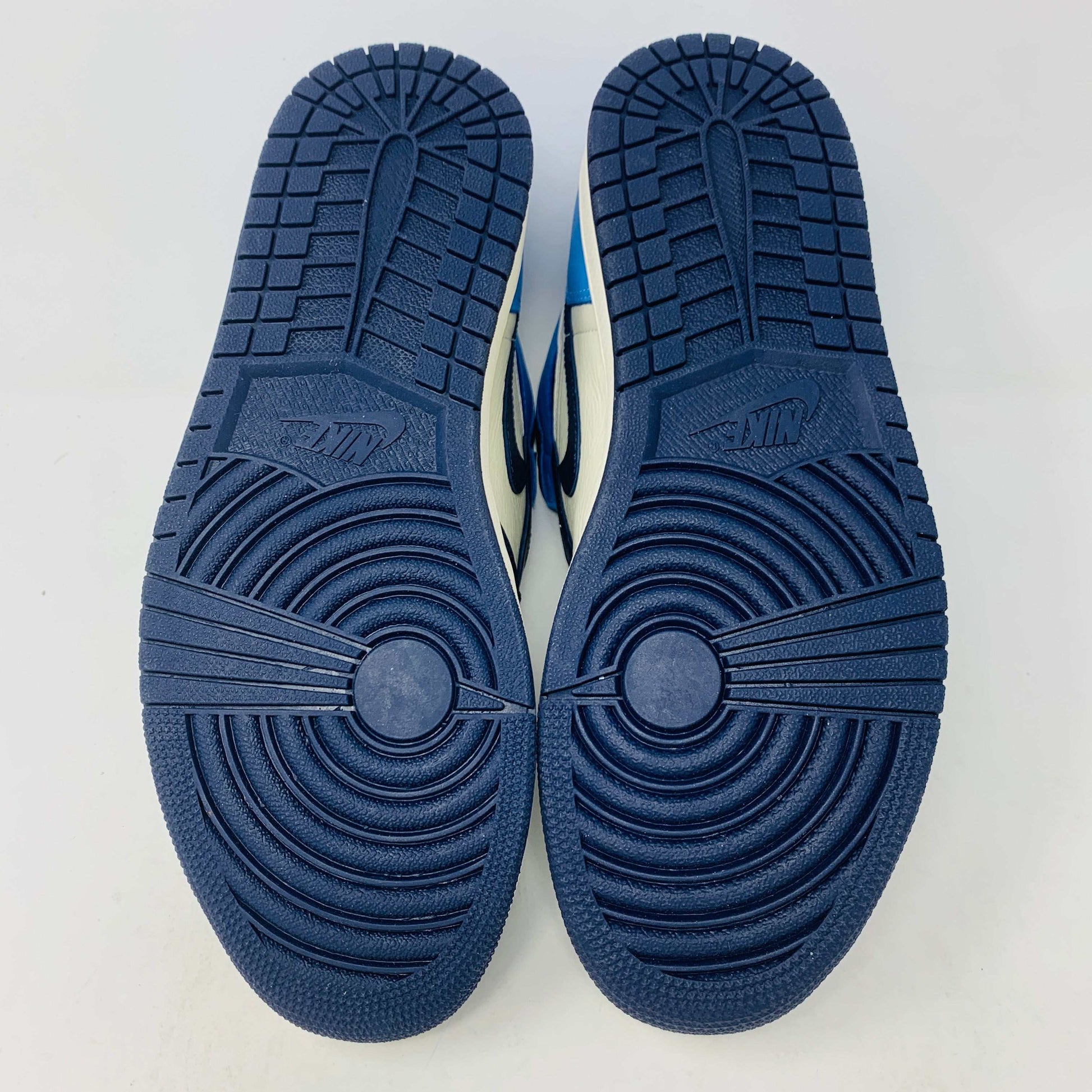 The new Jordan 1 Obsidian high-top sneaker, in blue and white with a black swoosh and blue laces, is displayed on a black and red box featuring 1985 Air Jordan 1 text. A printed Air Jordan wings logo is near the ankle.