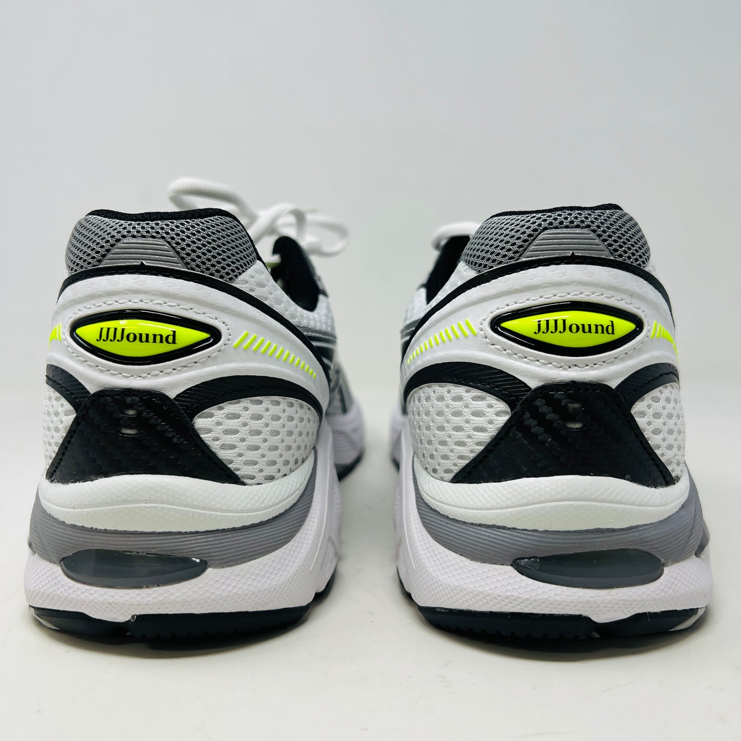 A brand new pair of ASICS GT-2160 JJJJound White sneakers, featuring mesh details and black stripes, is displayed on a black ASICS shoe box with extra laces in front for a complete authentic look.
