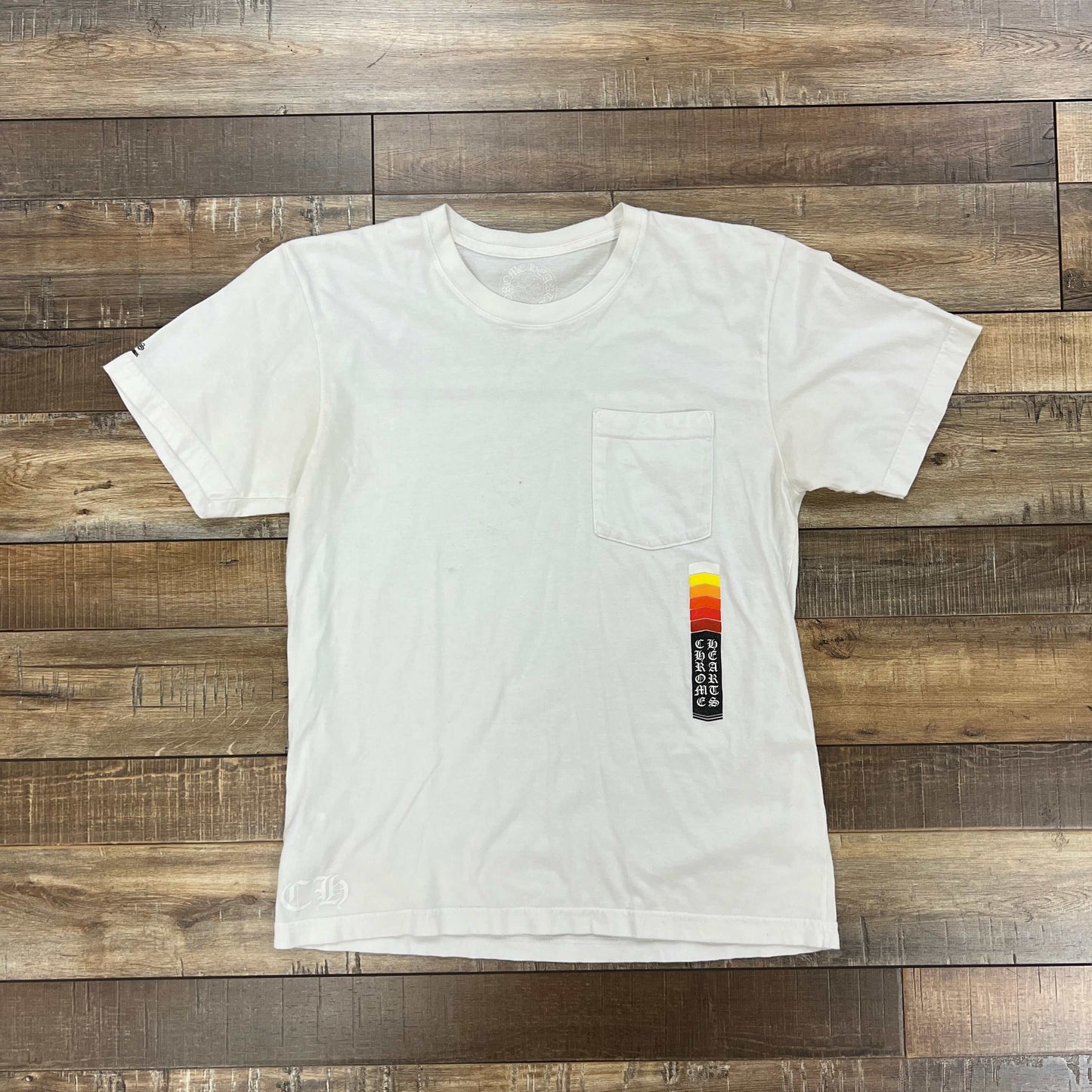 White preowned Chrome Hearts Boost T-Shirt with small chest pocket and vertical colorful graphic on wooden floor background